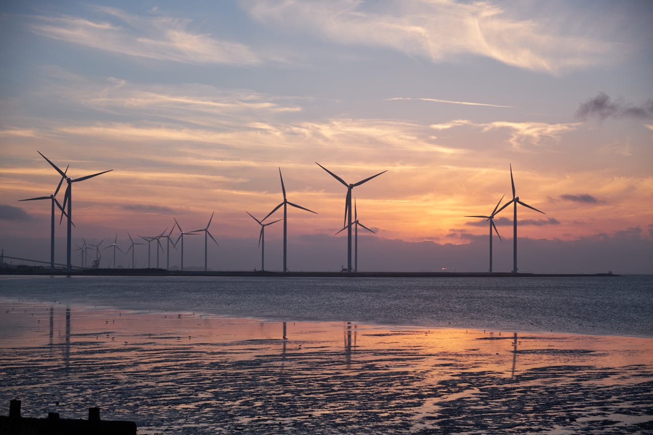 Home Wind turbines on the shoreline silhouette against a vibrant sunset, promoting renewable energy.